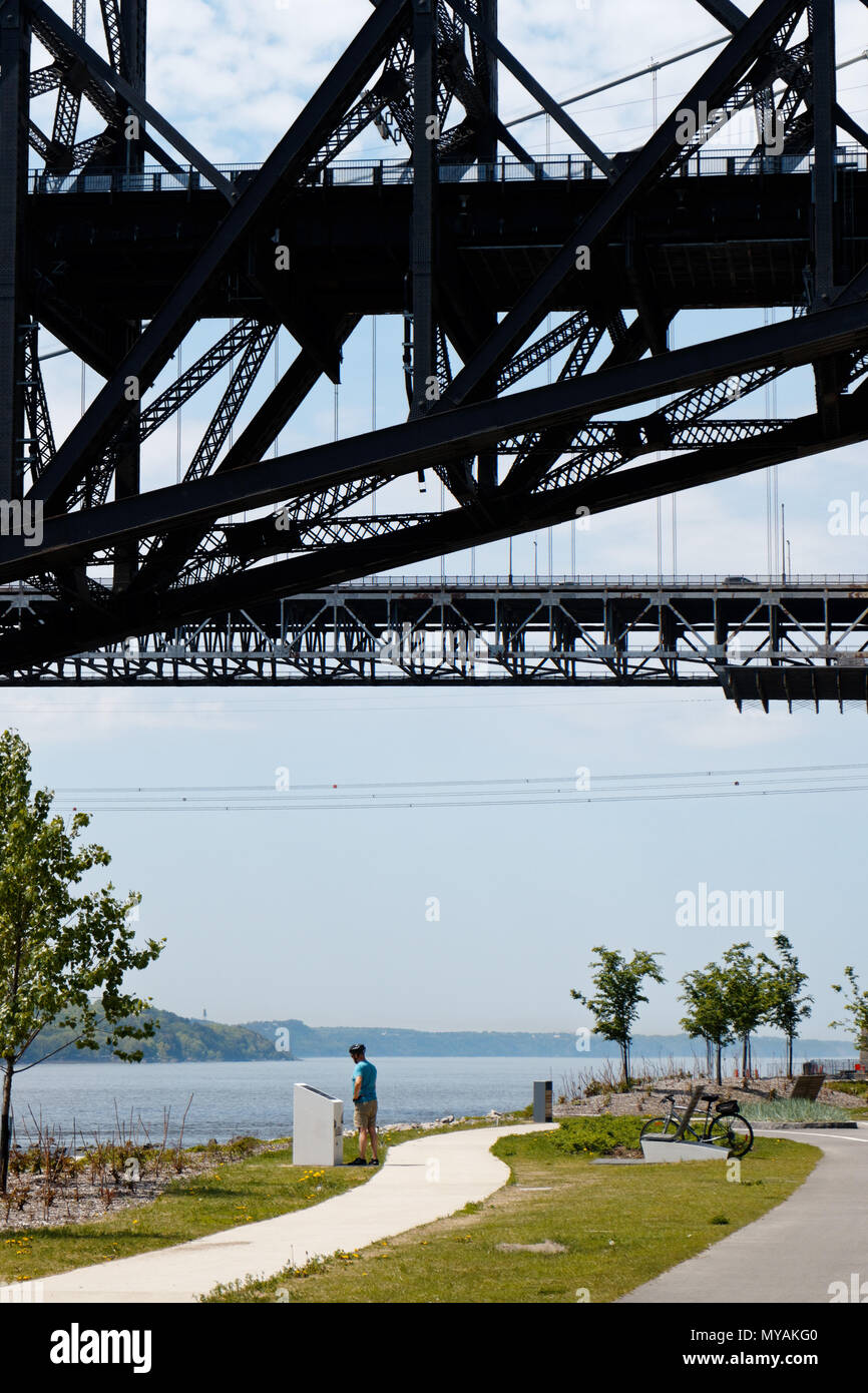 A cyclist relaxing on the Promenade Samual de Champlain cbike path in Quebec City, Canada with the Pont du Quebec overhead Stock Photo