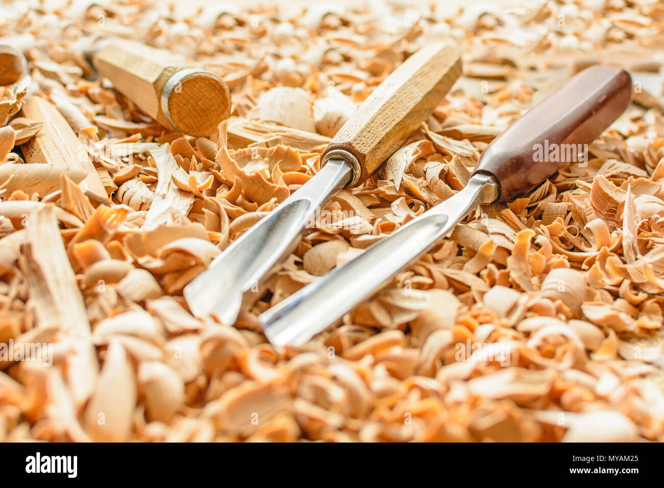 Chisels laid in wooden shavings on the desk. Carving tools lying in the shavings. In a carving workshop. Cutting of linden wood. Stock Photo