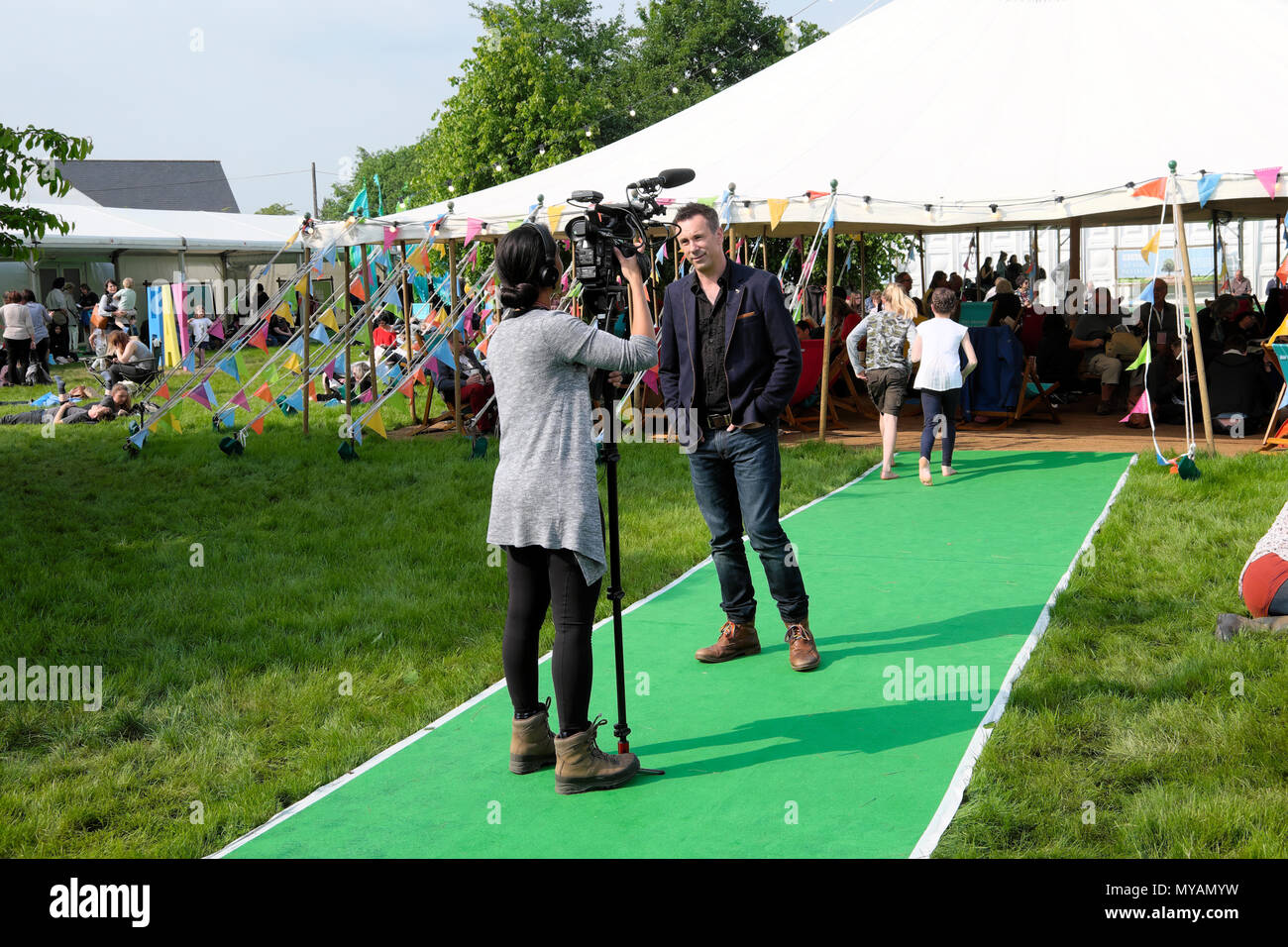 Rear view of young woman filming @BBCclick presenter Spencer Kelly at the Hay Festival site in sunshine in May 2018 Hay-on-Wye Wales UK  KATHY DEWITT Stock Photo