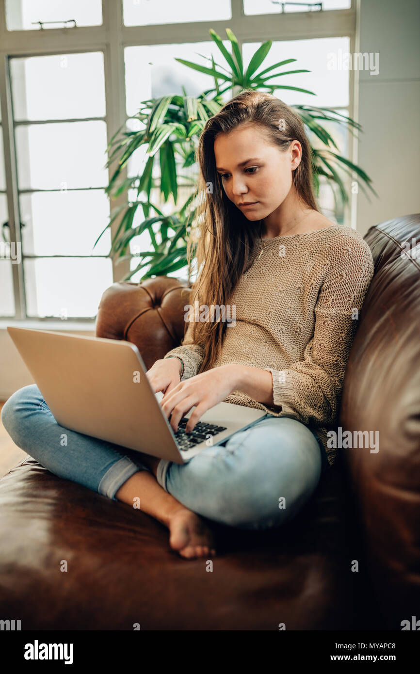 Woman sitting on a sofa at home with legs crossed and working on a ...