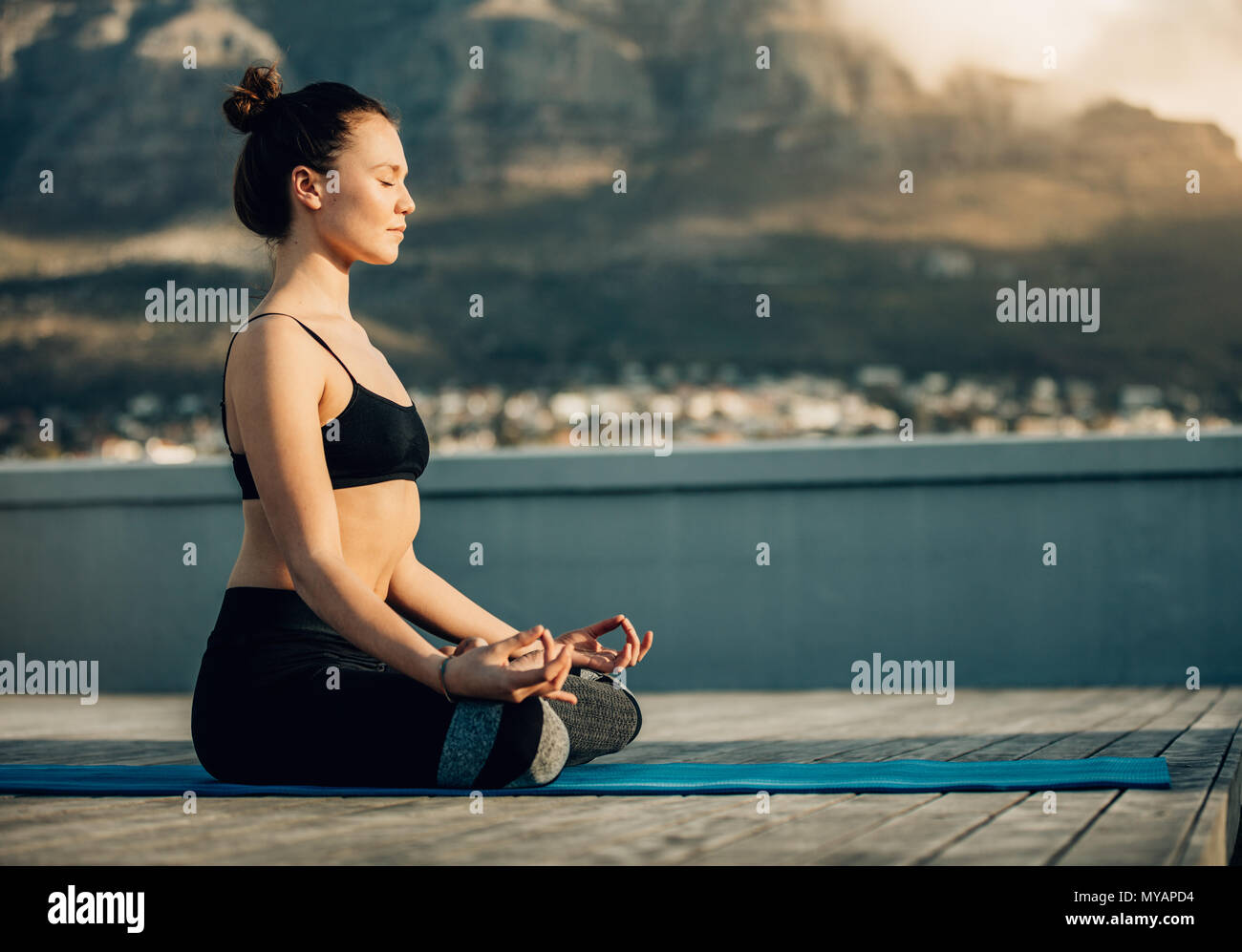 Woman practicing yoga on the terrace of her home. fitness woman meditating in a yoga posture sitting on the floor with legs crossed. Stock Photo