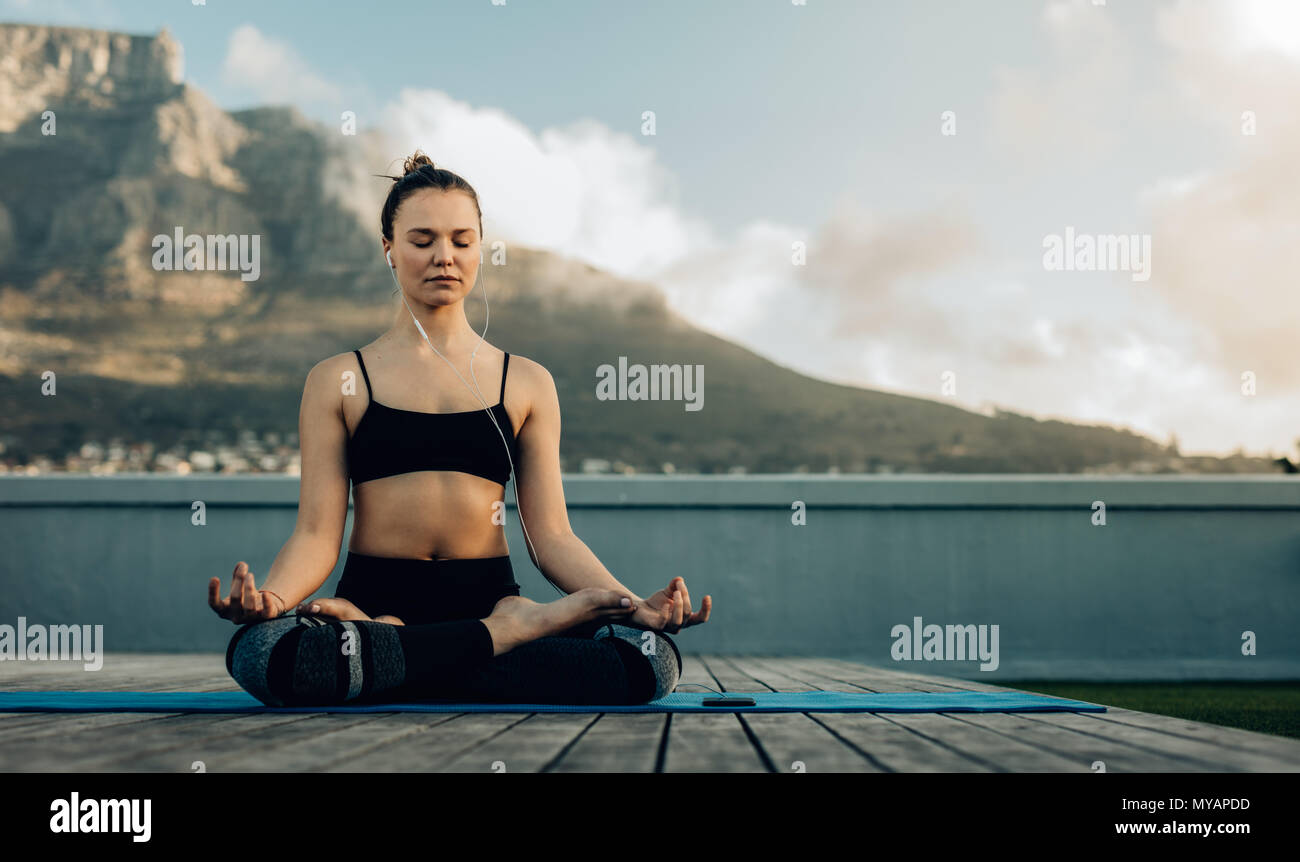 Woman practicing yoga on the terrace of her home. fitness woman meditating in a yoga posture sitting on the floor with legs crossed and listening to m Stock Photo