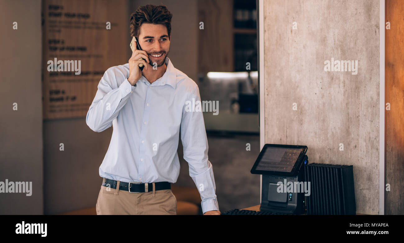 Young businessman standing in a cafe and talking on phone. Restaurant manager making a phone call. Stock Photo