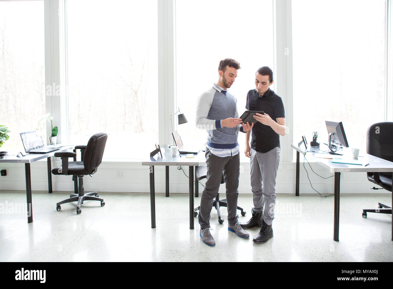 Two young businessmen in an office look at a tablet computer. Stock Photo