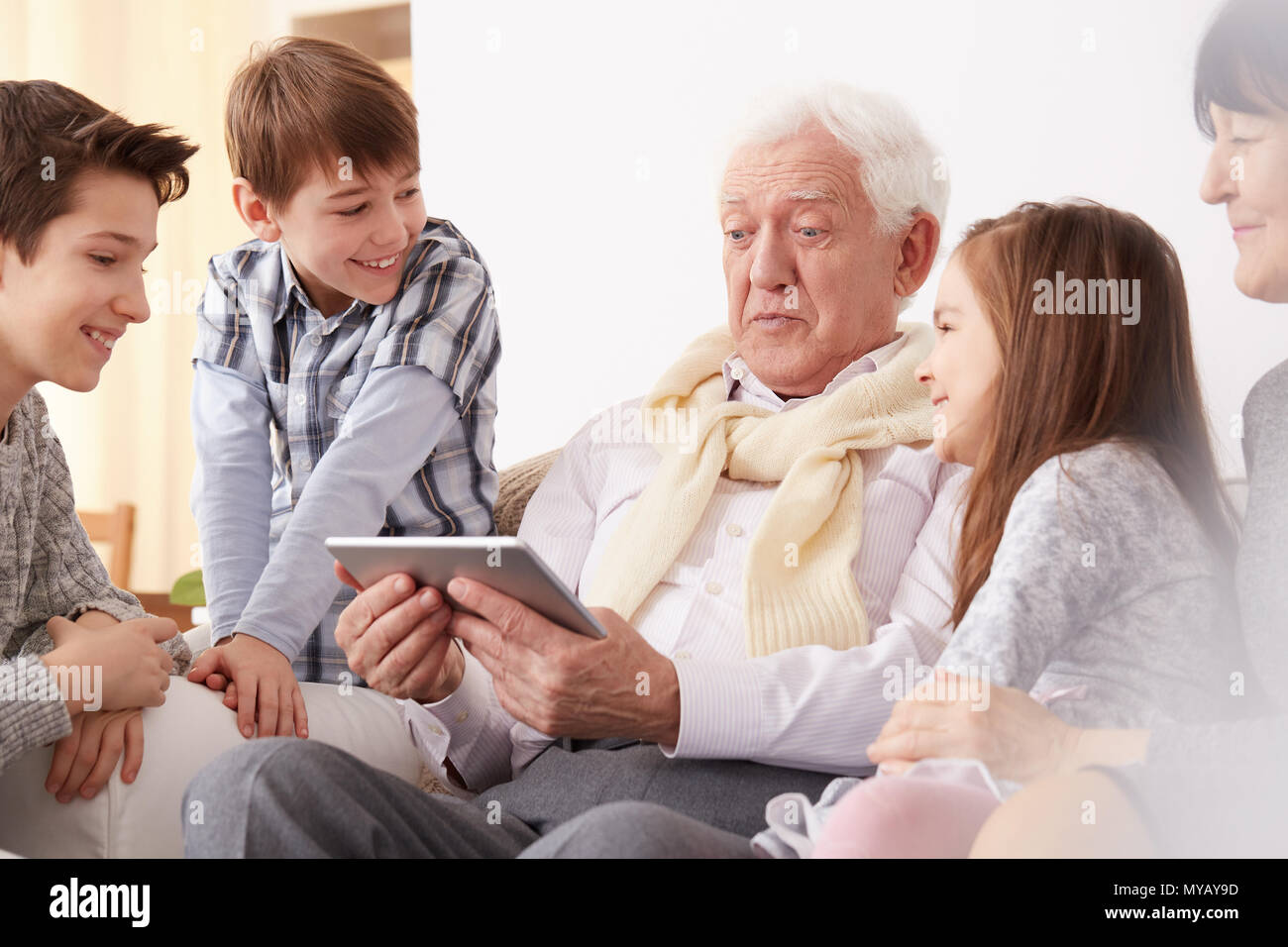 Happy children looking at their surprised grandpa holding a tablet Stock Photo