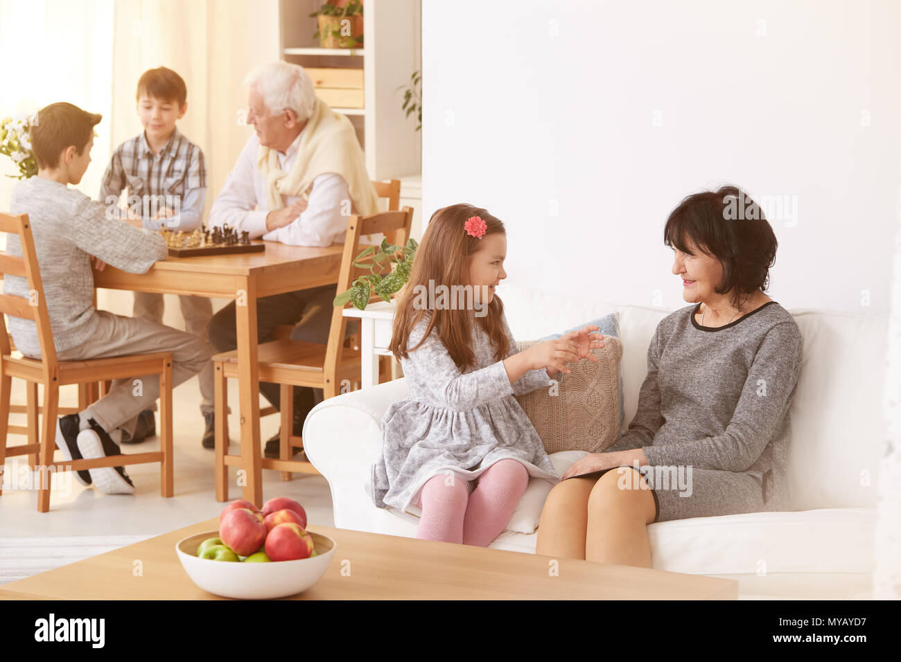 Grandma talking with granddaughter and grandpa playing chess with grandsons Stock Photo