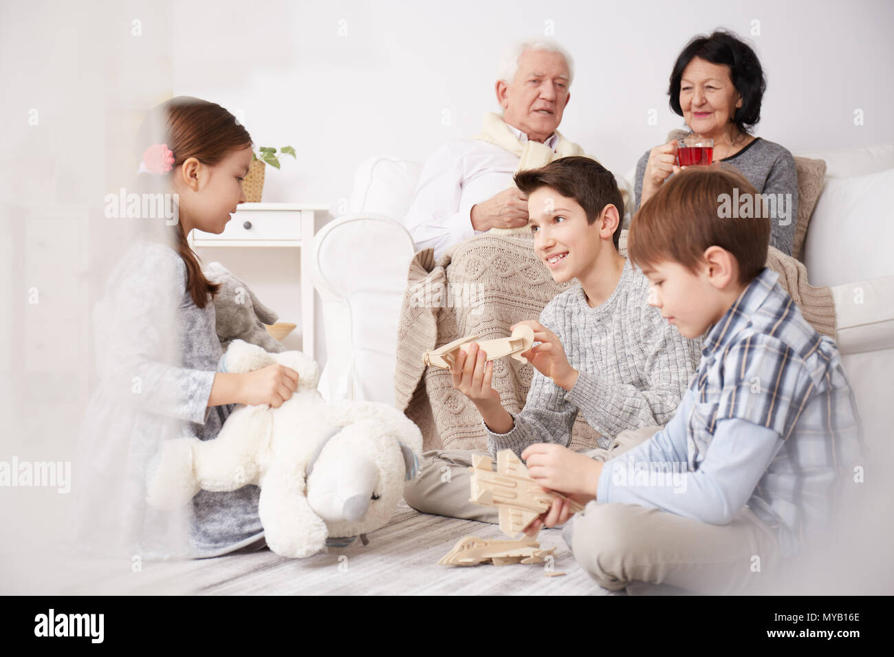 Children playing on a floor and their grandparents sitting on a sofa Stock Photo