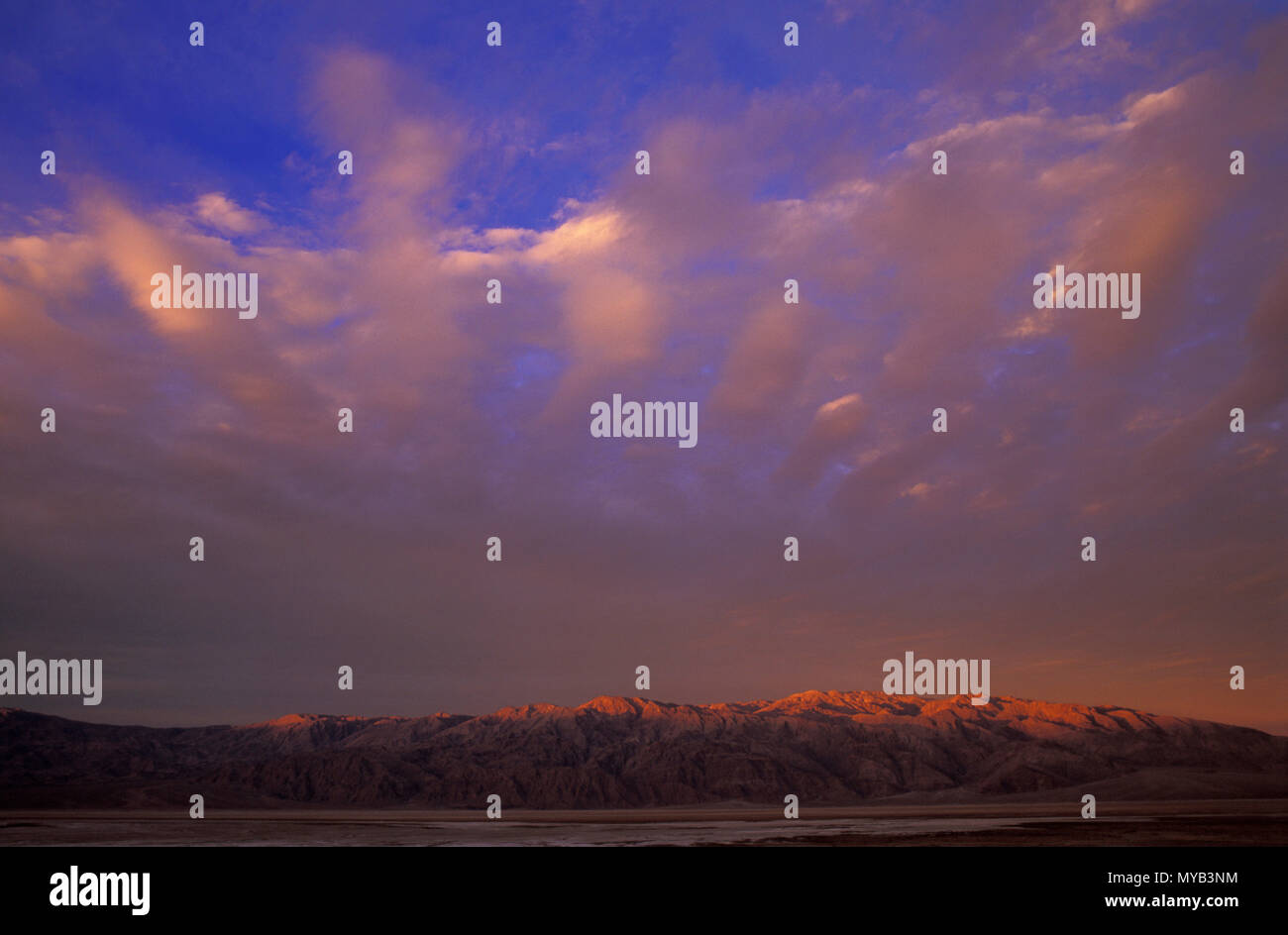 Sunrise in Death Valley, with sun just reaching mountain range with dramatic cloud pattern, Death Valley, CA, USA Stock Photo