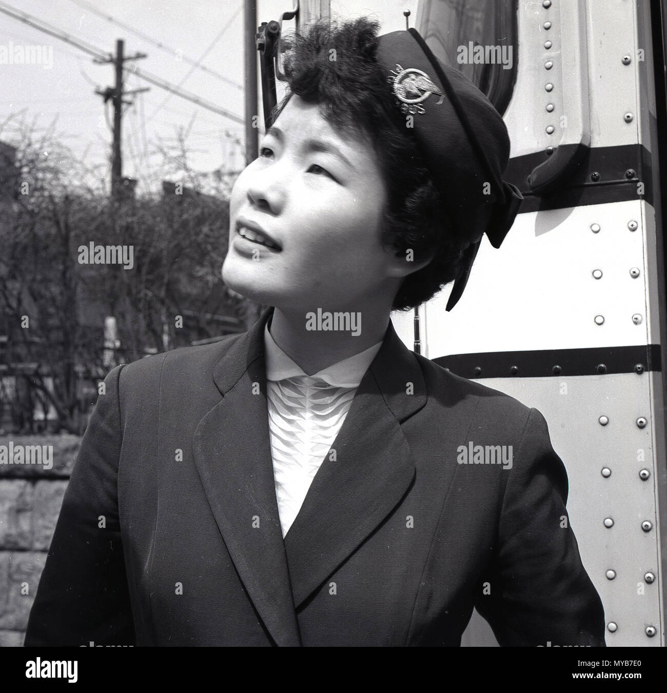 1950s, historical, close-up picture of a Japanese female Tourist guide wearing uniform and hat standing outside her tourist coach in Tokyo city centre, Japan. These guides were female personnel who travelled with the tourists on the coach and pointed out various parts of the city and were there to help generally the overseas visitors. Stock Photo