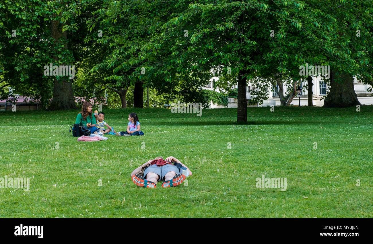 A man lying flat on grass, completely relaxed, woman sitting with children in area behind him, St James's Park, London, England, UK Stock Photo