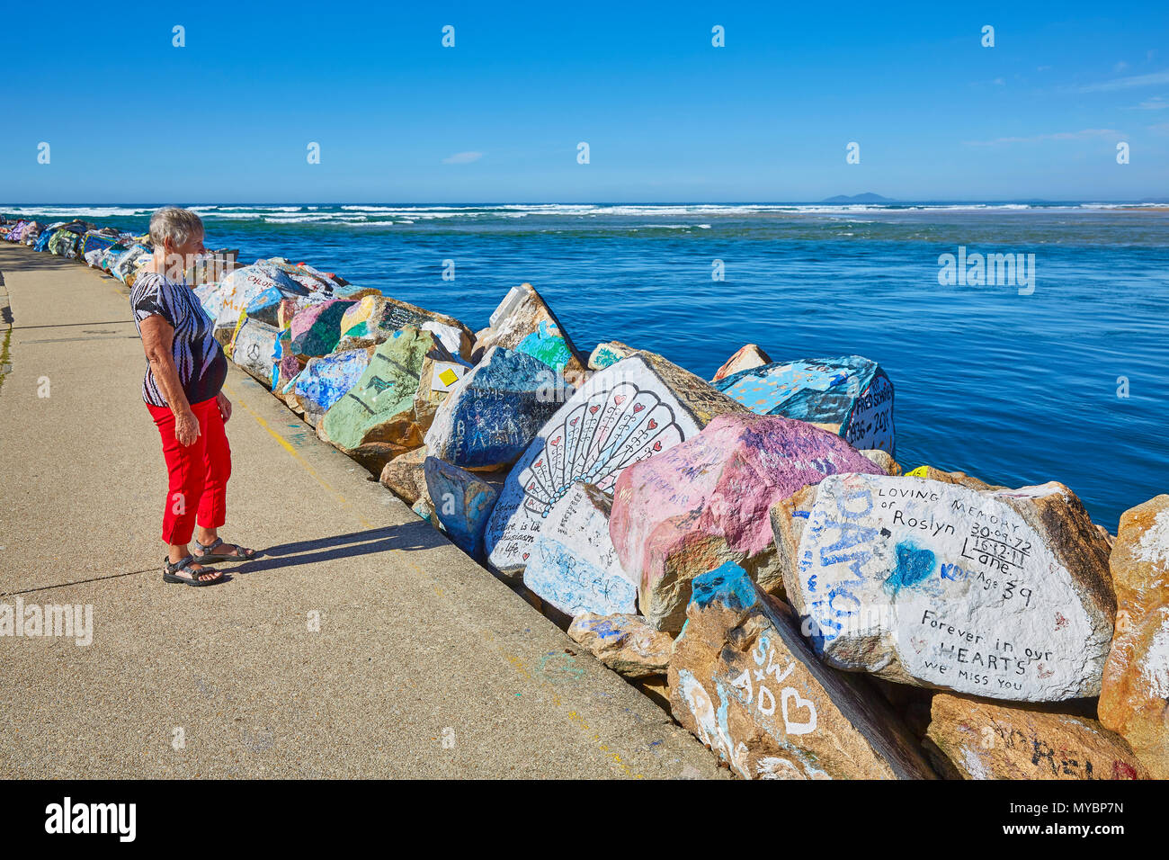 A woman on her own looking at the boulders decorated with signs and messages at the Vee Wall, Nambucca Heads, New South Wales, Australia Stock Photo
