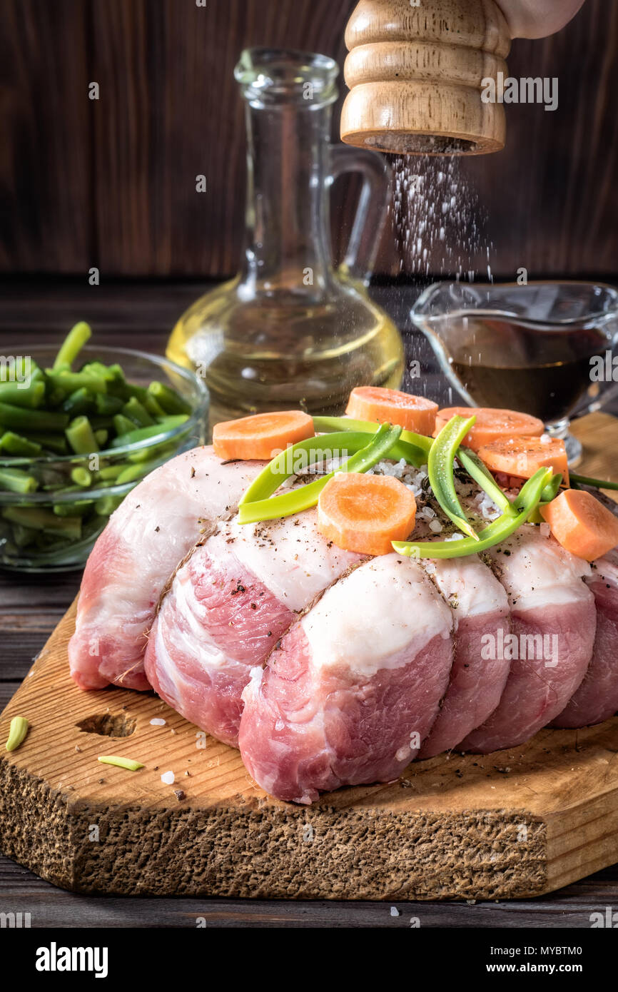 Raw pork chop meat roll wrapped twine jute marinated strew coarse sea salt shaker mill olive oil with pepper assorted vegetables with carrots green on Stock Photo