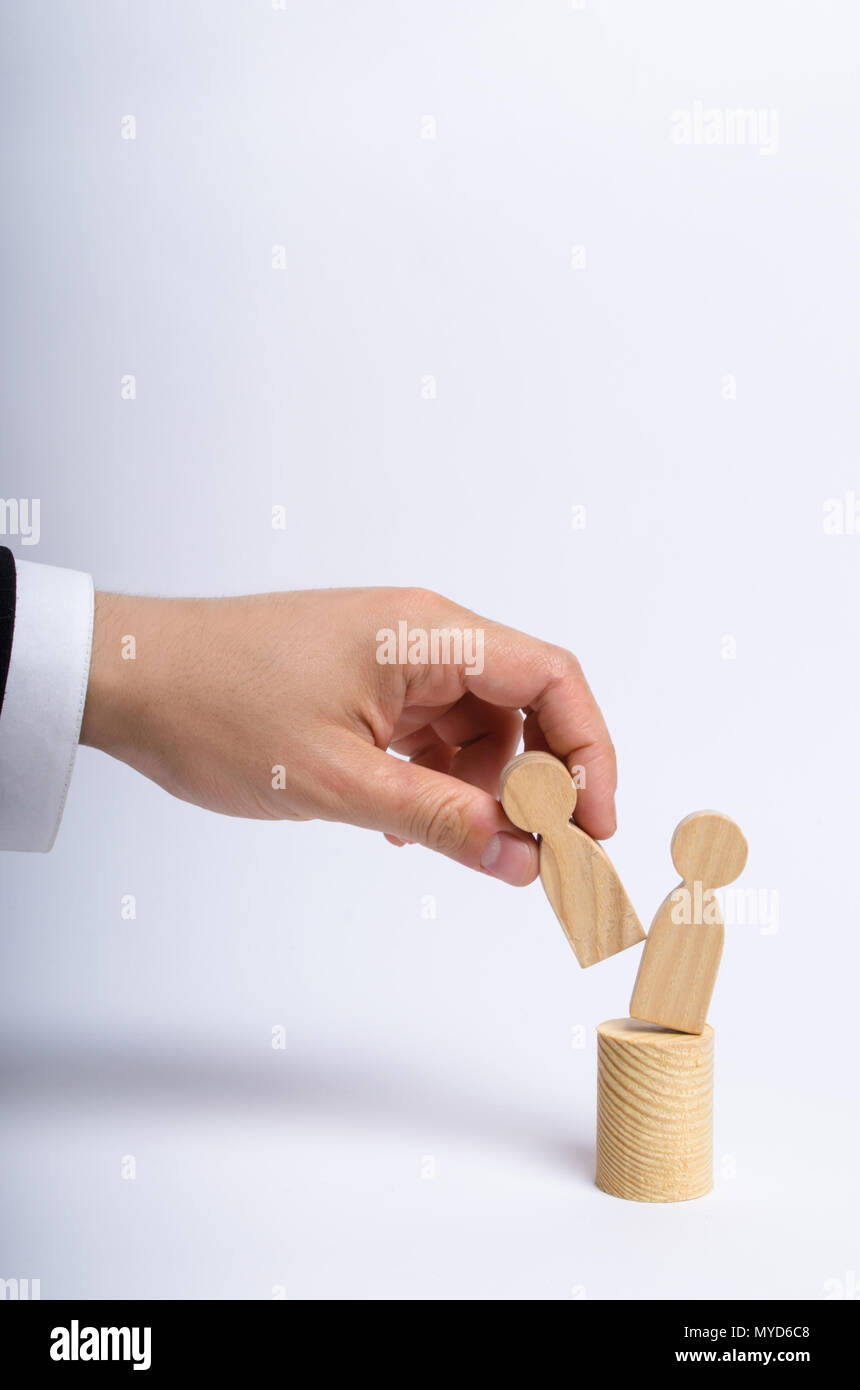 The man's hand of a businessman in a business suit holds a wooden figure of a man in his hand and moves another figure from his post. The concept of f Stock Photo