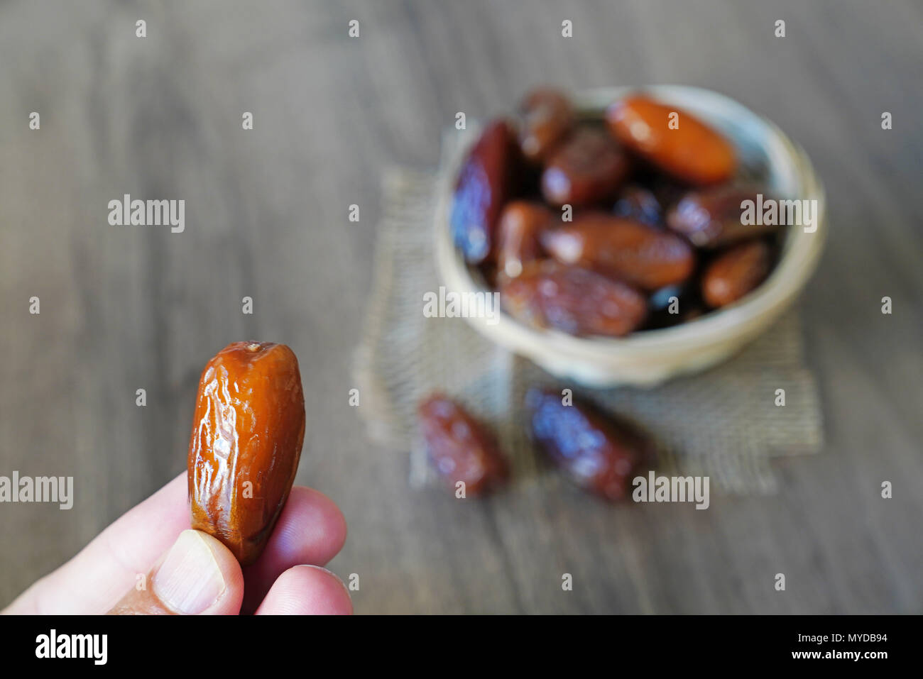 Human finger holding single date fruit and blurred dates filled bowl in background Stock Photo