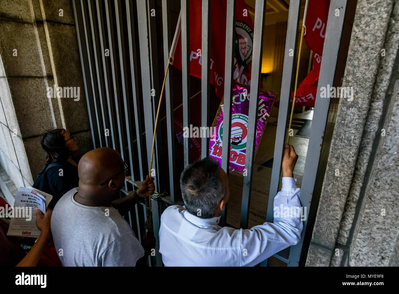 June 6, 2018 - London, UK. 6th May 2018. IWGB members and supporters poke flags through the locked gates to the Senate House at the University of London. Over 100 cleaners, porters, security officers, receptionists, gardeners, post room staff and audiovisual staff were on strike today and were joined by supporters for a lively rally. The Independent Workers Union of Great Britain is the largest union in the University of London central administration buildings but its members there are employed by a number of outsourcing companies, working with worse pension, holiday pay, sick pay, maternity Stock Photo