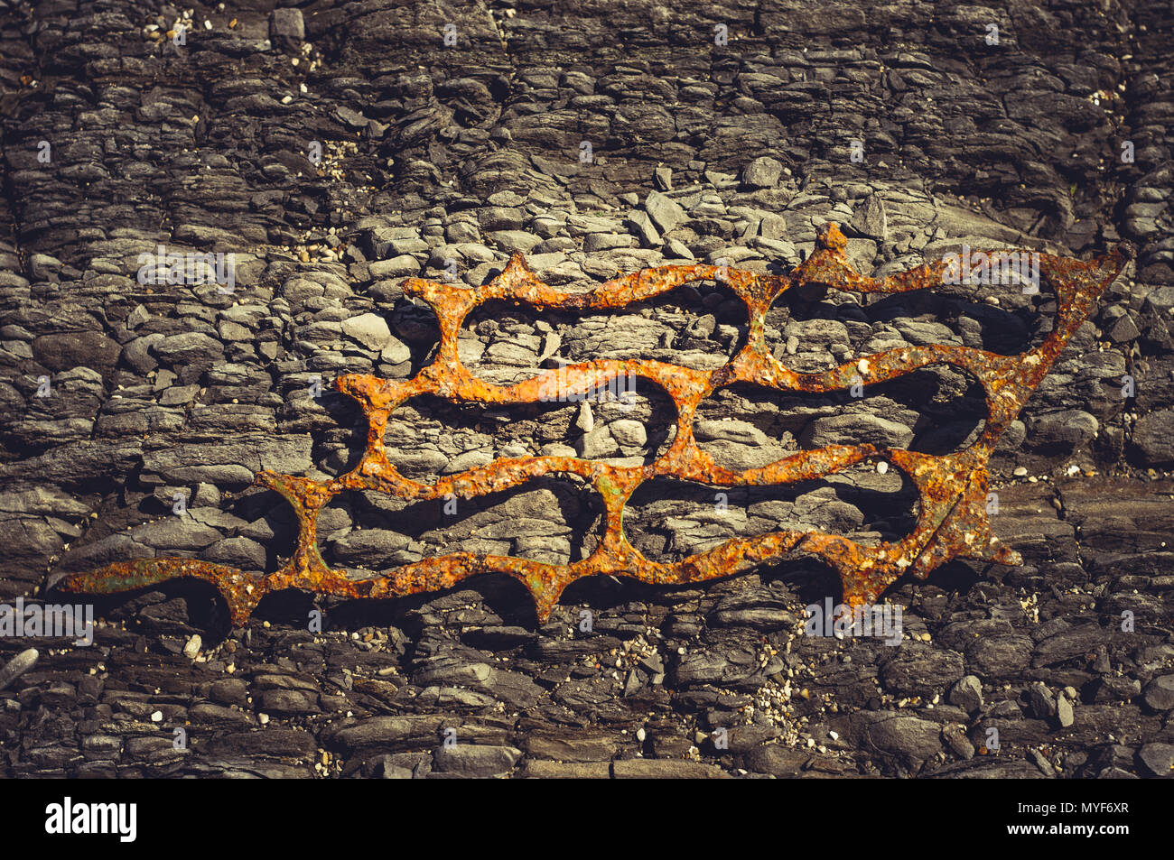 Very rusty metal on a gray cracked rock, bright sunlight, close up ...