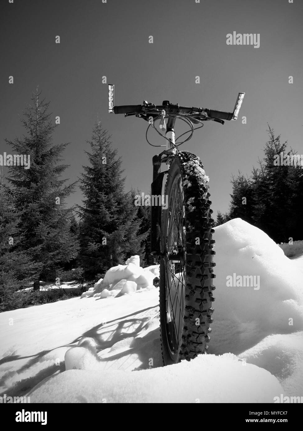 Close wide view to mountain bike stays in snow. Winter snowy mountains with road between trees. Stock Photo