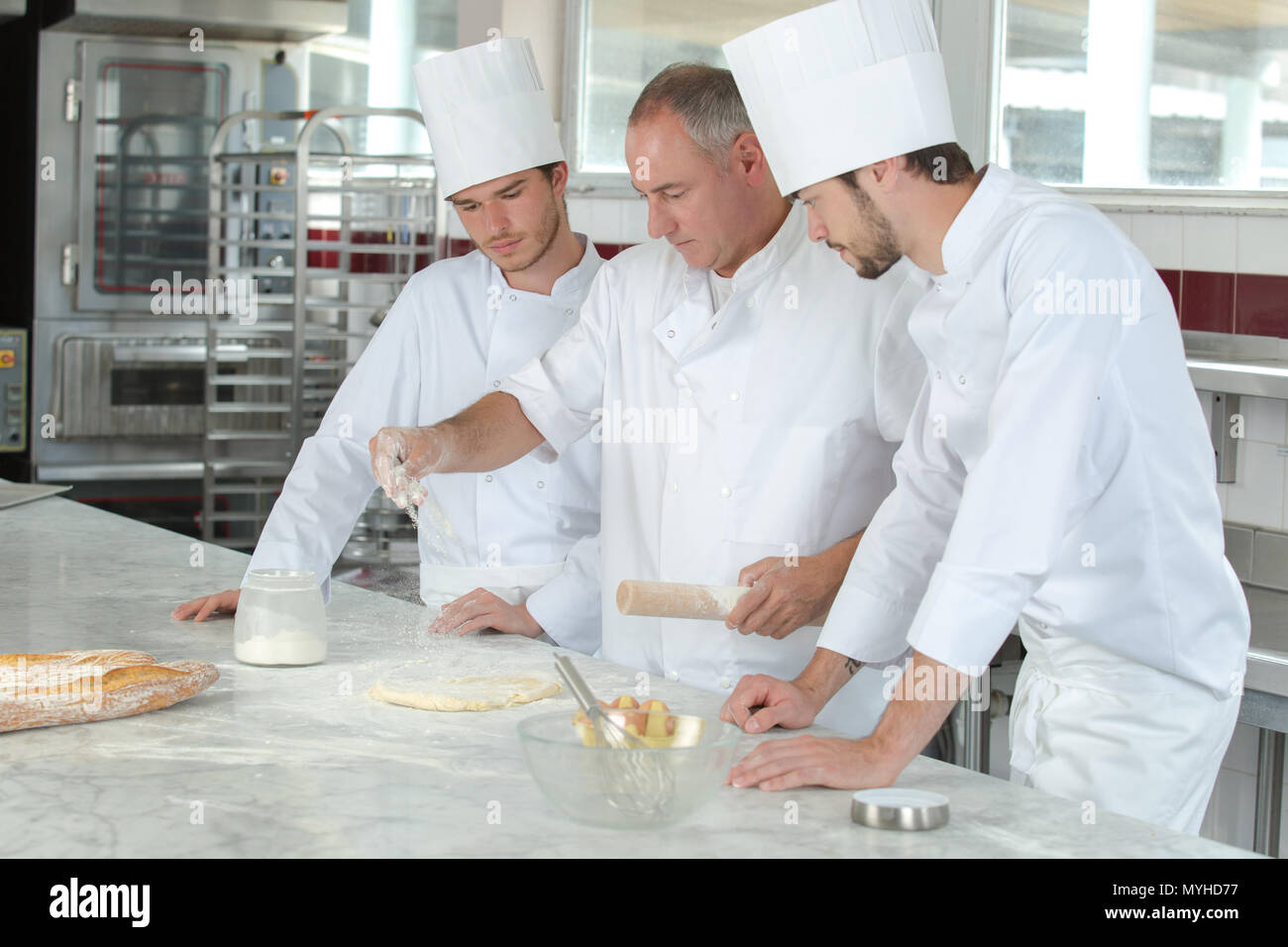 three bakers wearing work coats and baking Stock Photo Alamy