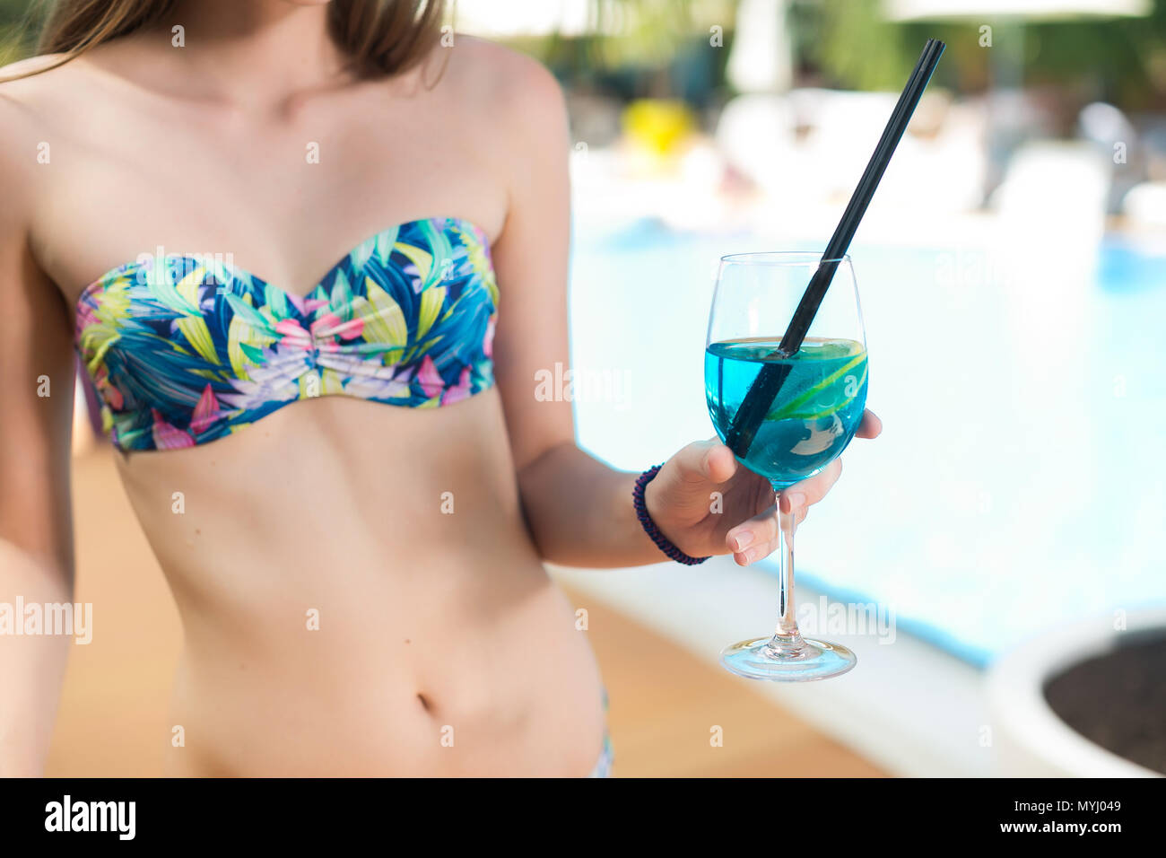 summer, vacation, holidays concept. close up of girl hand with unnatural bright blue cocktail with black straw, holden by thin elegant girl dressed in bikini in the same blue colour Stock Photo