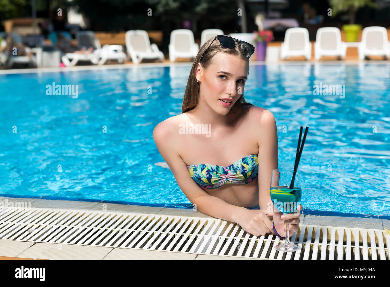 fashion, appearance, enchantment concept. by the edge of pool there is girl who is half dip in the clean water, she is swimming and having fun, drinking cocktails Stock Photo