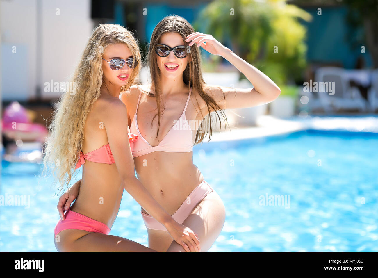 vacation, lifestyle, sex concept. there are two girlfriends, models, they are posing and holding each other, smiling at the camera surrounded with palm trees and summer sunlight Stock Photo