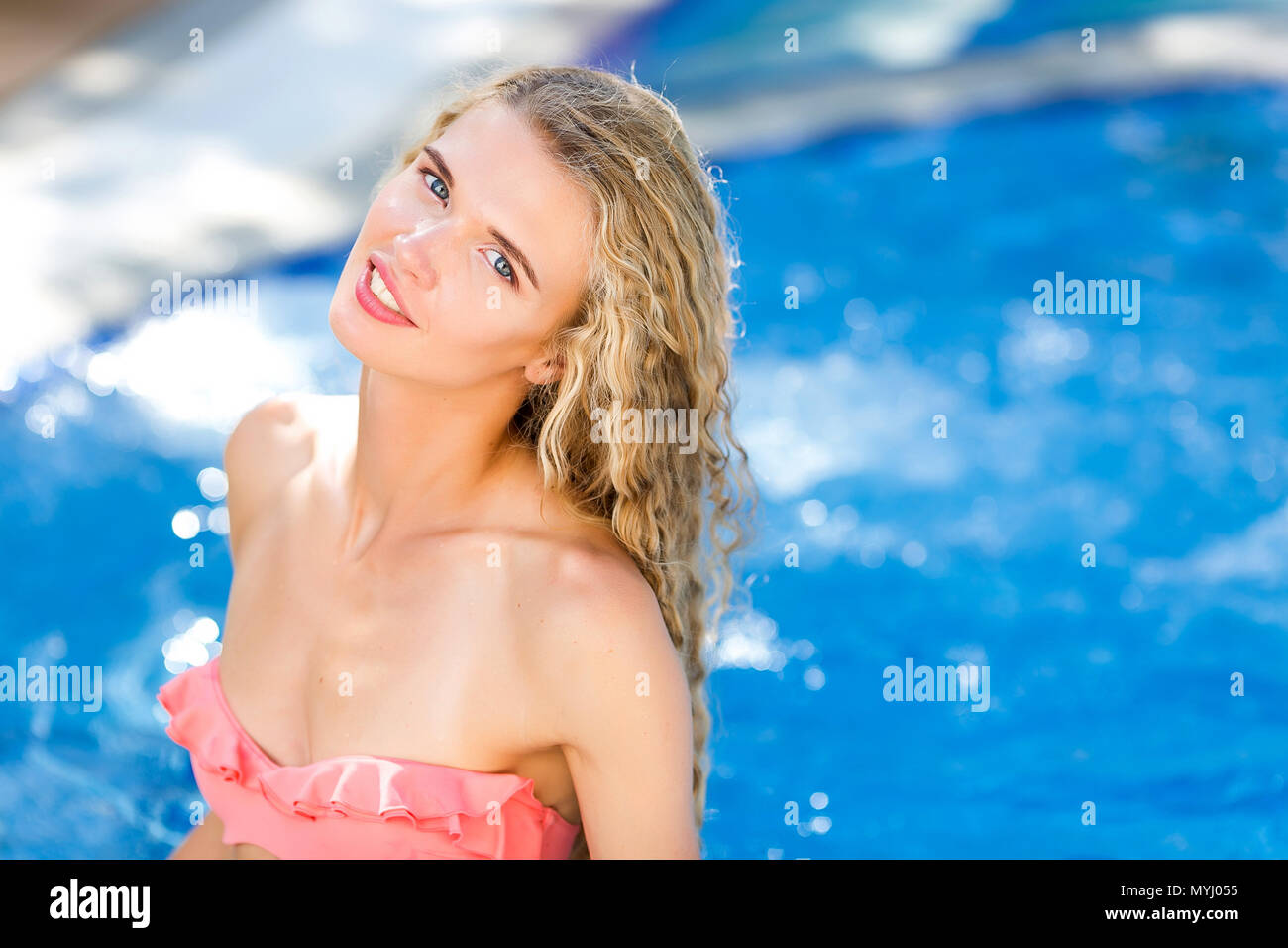 charm, fashion, gladness concept. portrait of pretty girl with charming smile, she is standing in the water of swimming pool and looking with foxy eyes and her hand bent Stock Photo