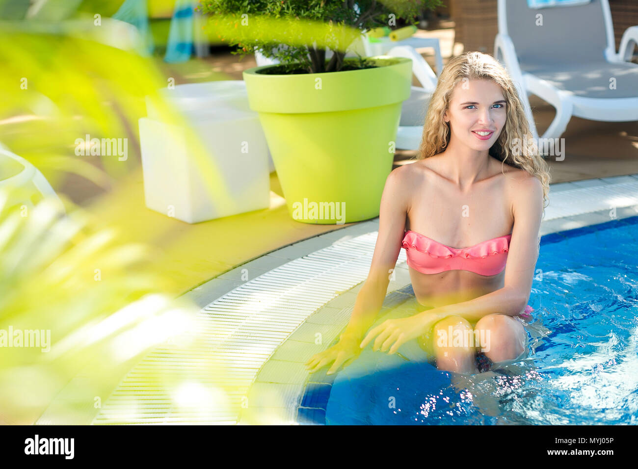hotel, tourism, resort concept. young girl is sitting in the swimming pool by this edge where placed a huge pot with some tree and a few deck chairs Stock Photo