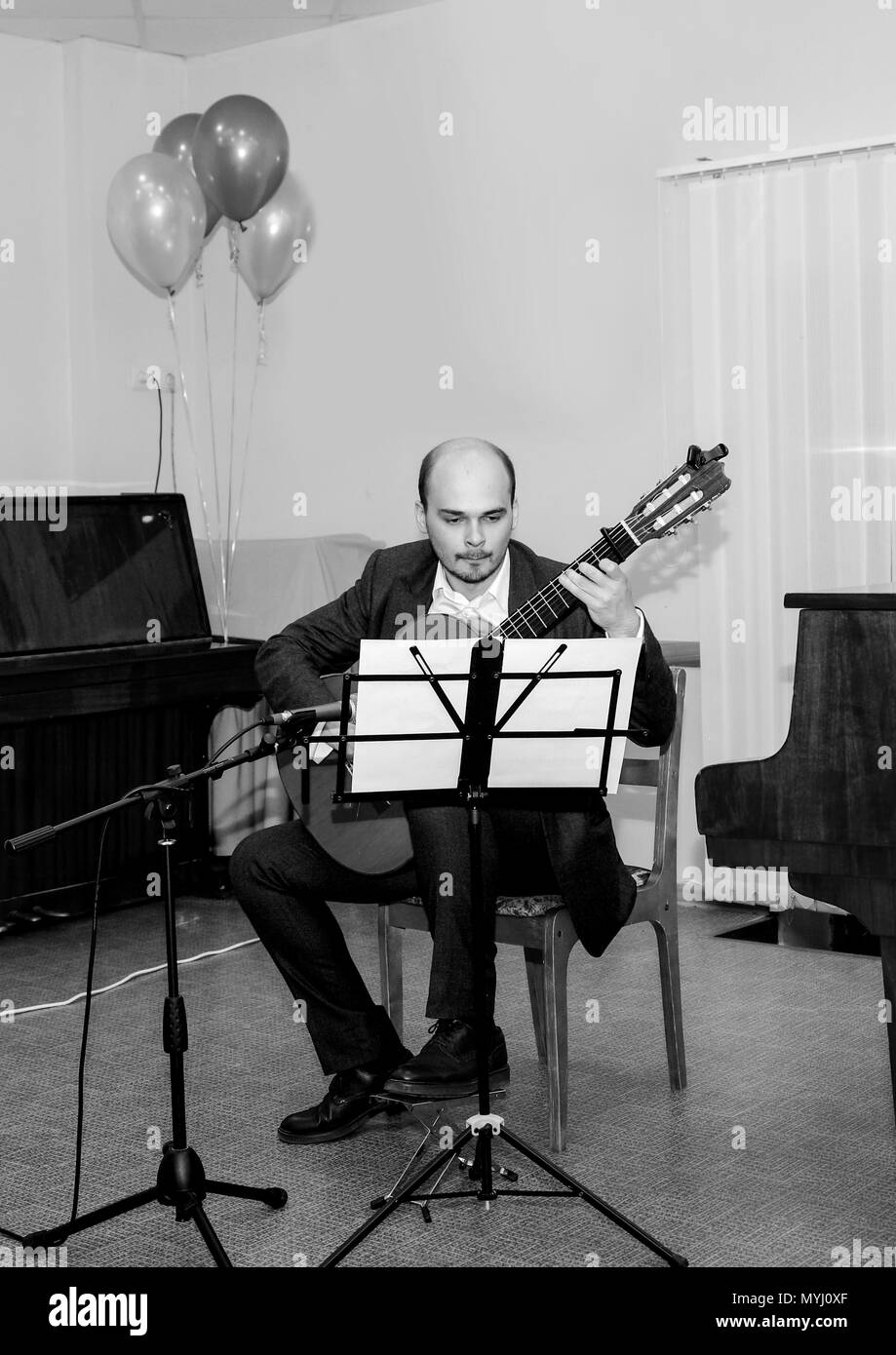 Black and white photo. The musician looks at the notes and plays the guitar. Stock Photo