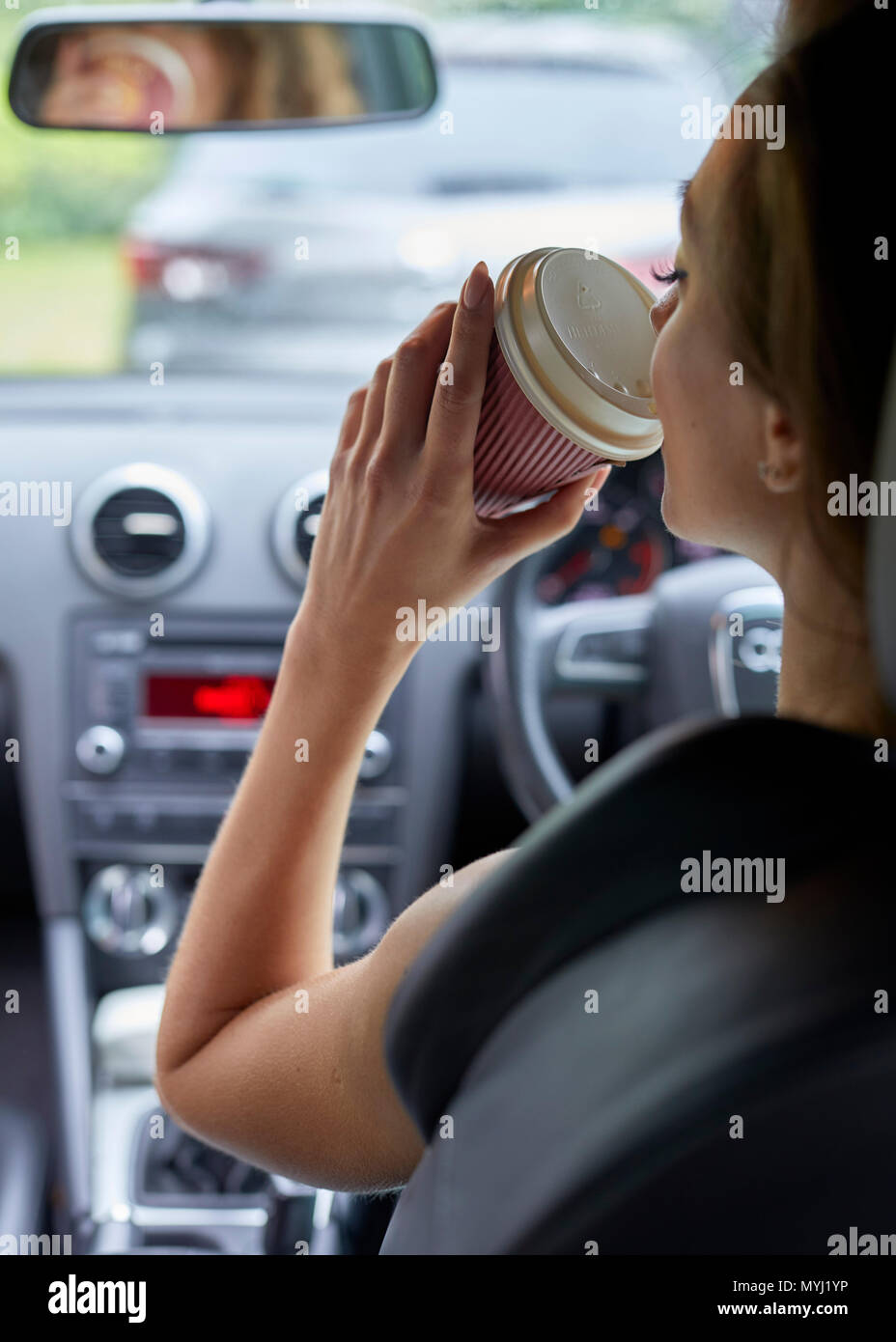 Woman drinking coffee whilst driving Stock Photo