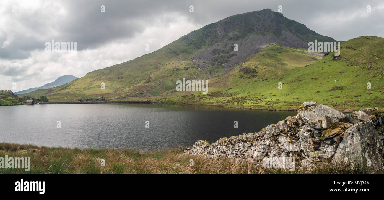 A dry stone wall leads to the fishing lake of Llyn Y Dywarchen in the Snowdonia National Park. The beautiful mountain y Garn is in the distance. Stock Photo