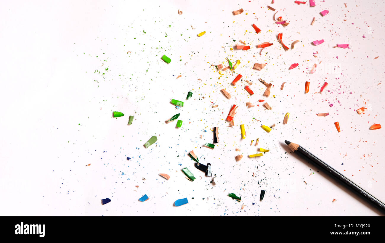 Flat lay of black color pencil with colorful shavings scattered around, on a white paper background. Stock Photo