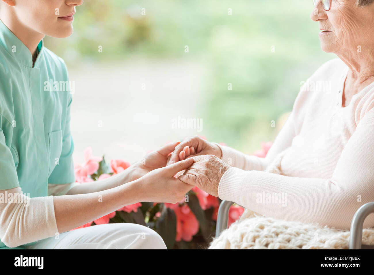 Nurse holding hands of disabled elderly woman in a wheelchair Stock Photo