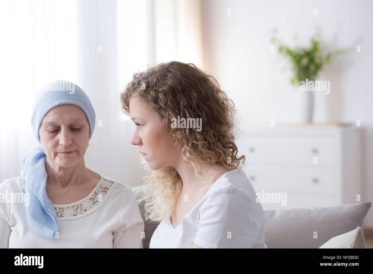 Sad senior woman with cancer wearing a blue headscarf during a meeting with caregiver Stock Photo