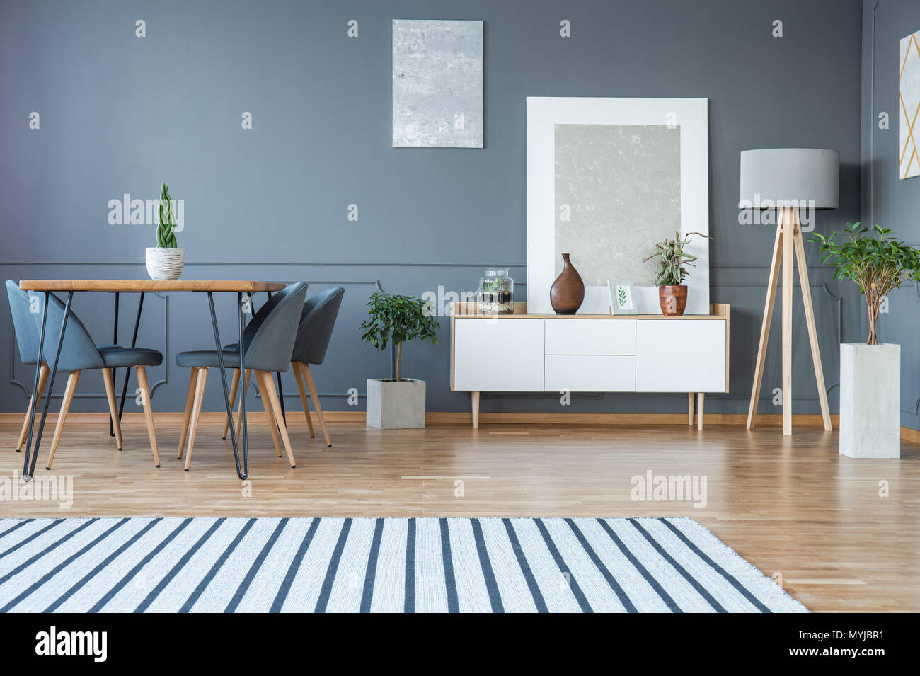 Modern dining room interior with a striped rug, table, grey chairs and white cabinet Stock Photo