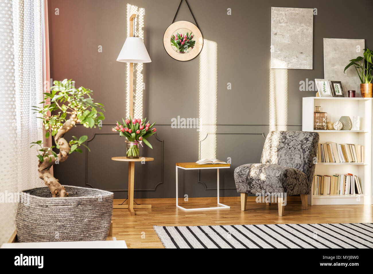 Bonsai tree in a fabric pot cover, tulips on a wooden table, bookshelf and  patterned armchair in living room interior Stock Photo - Alamy