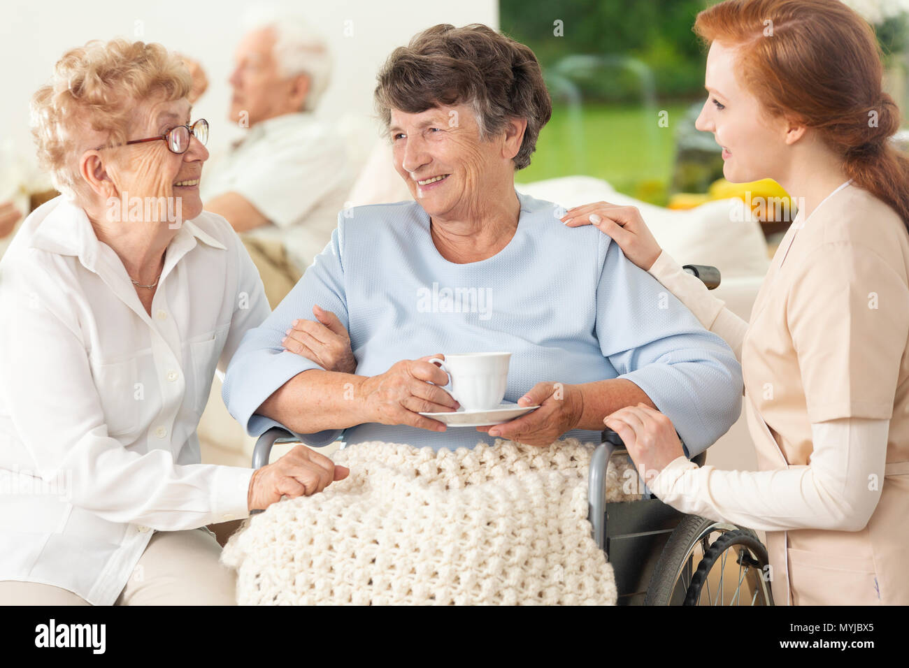 Smiling paralyzed senior woman between happy friend and nurse Stock Photo
