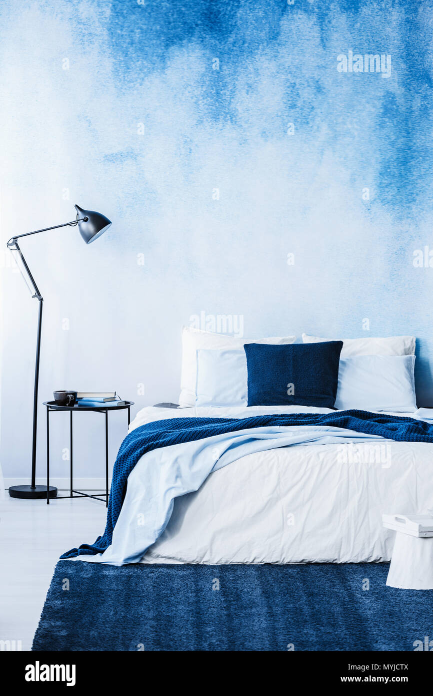 Navy blue carpet in front of bed next to lamp in bedroom interior with wallpaper Stock Photo