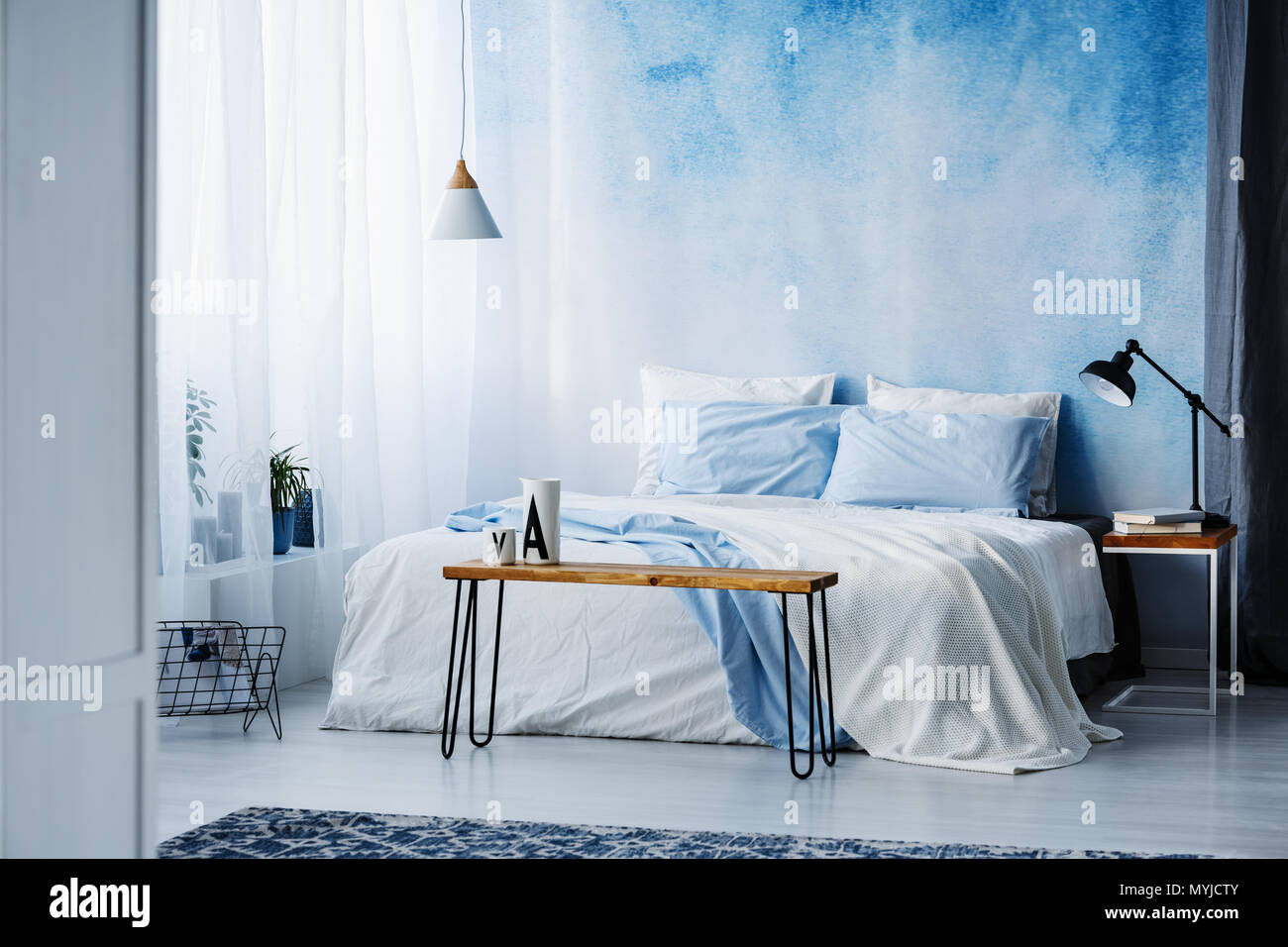Lamp on wooden table next to a blue and white bed in bedroom interior with ombre wall Stock Photo
