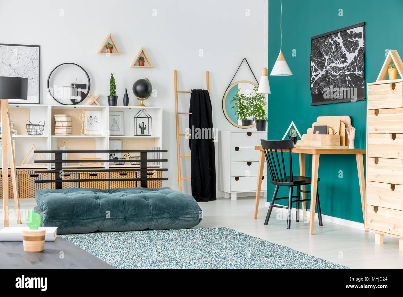 Black chair at wooden desk in kid's room interior with green mattress near patterned carpet Stock Photo