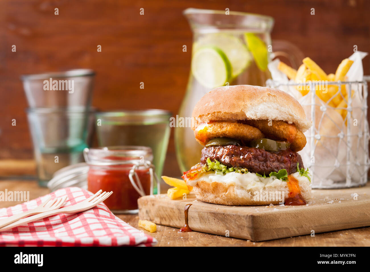 Burger in a bun with onion rings and fries on wooden background Stock Photo