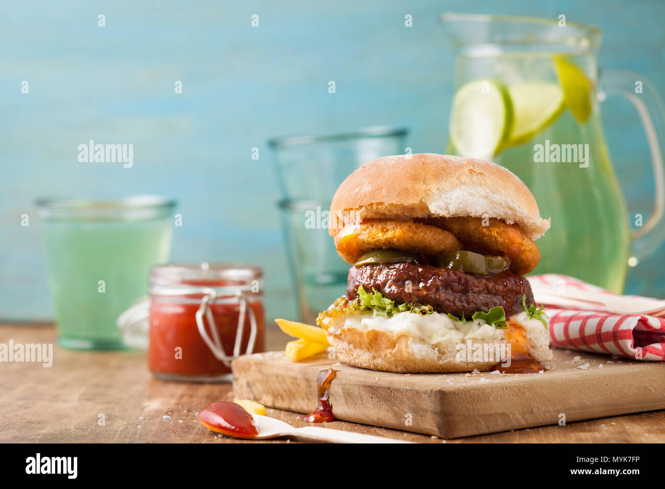 Burger in a bun with onion rings, chips and ketchup with a summery blue background Stock Photo