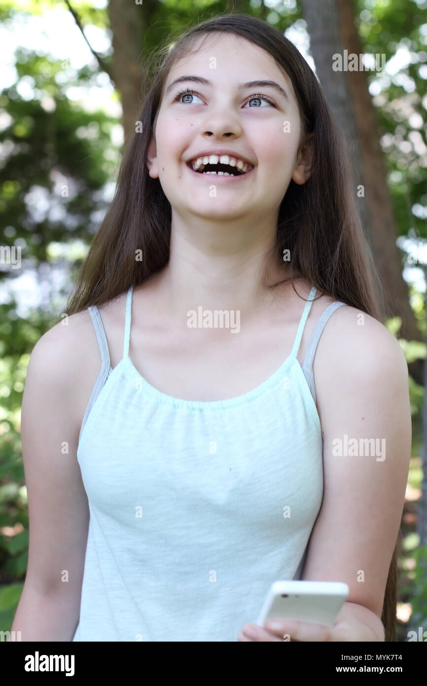 Happy laughing young teenage girl reading a text message on a smartphone. Selective focus on teen. Stock Photo
