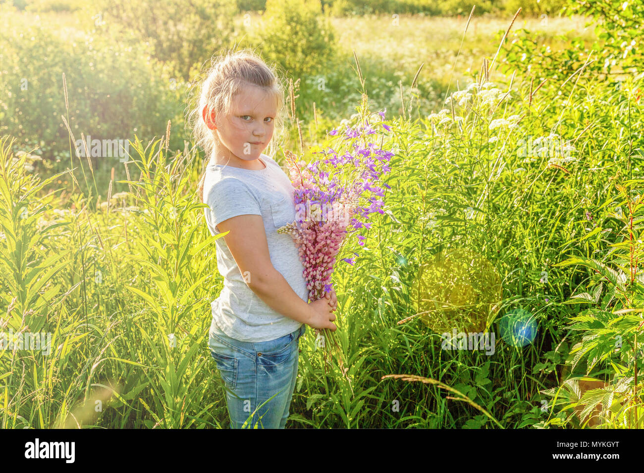 Happy cute little girl stands with a bouquet of wildflowers in the park ...