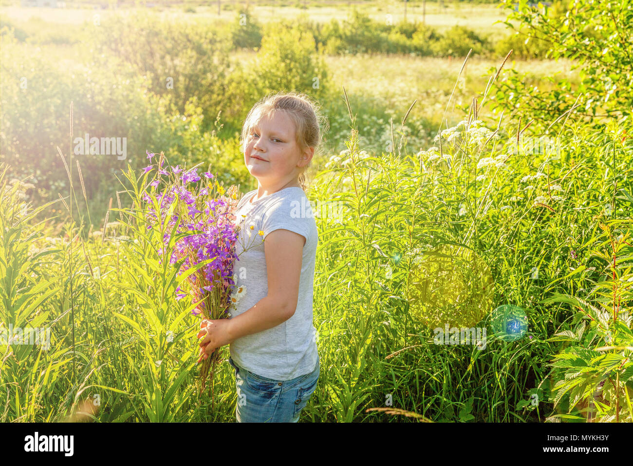 Happy cute little girl stands with a bouquet of wildflowers in the park ...