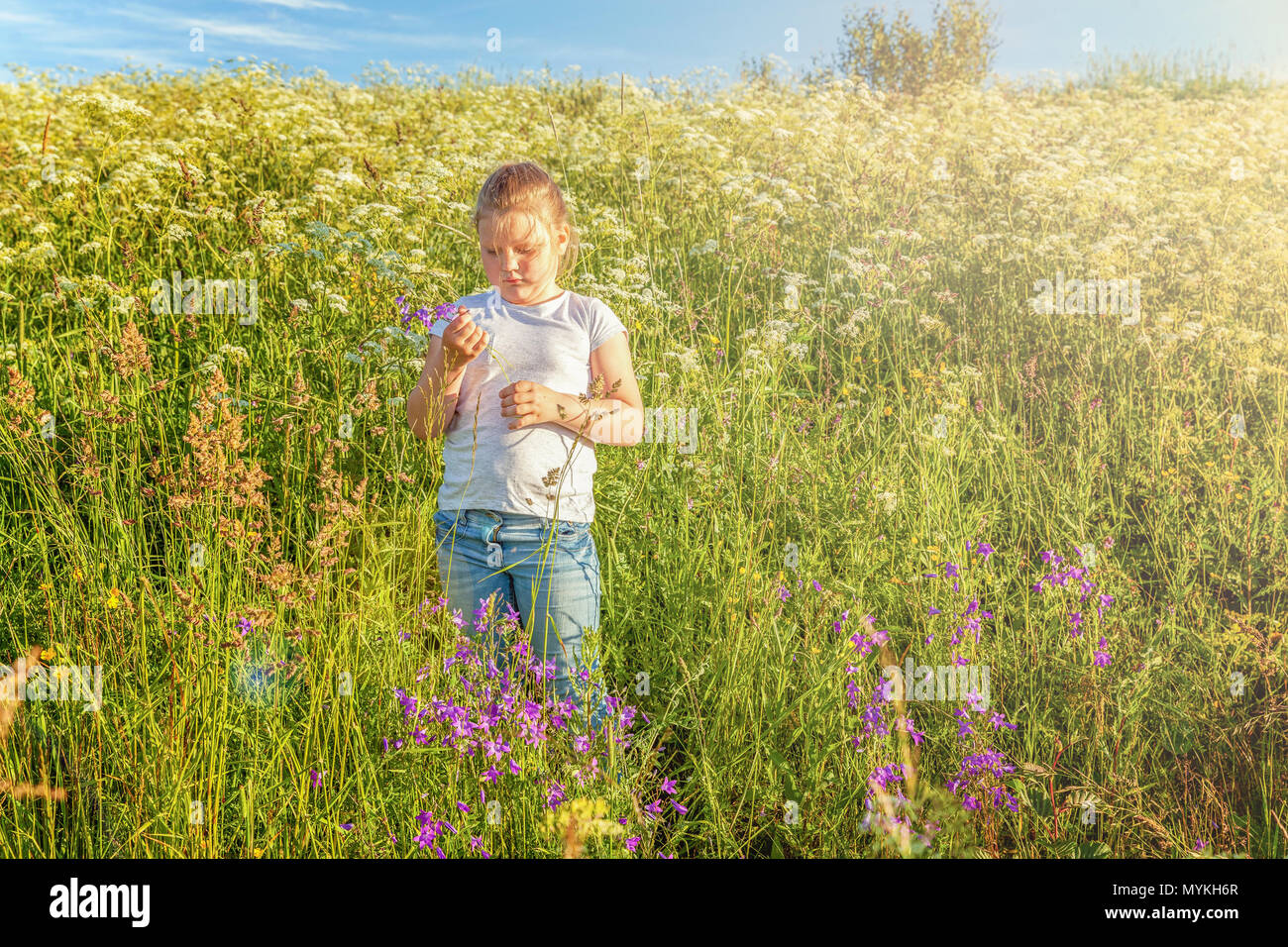 Happy cute little girl stands with a bouquet of wildflowers in the park ...