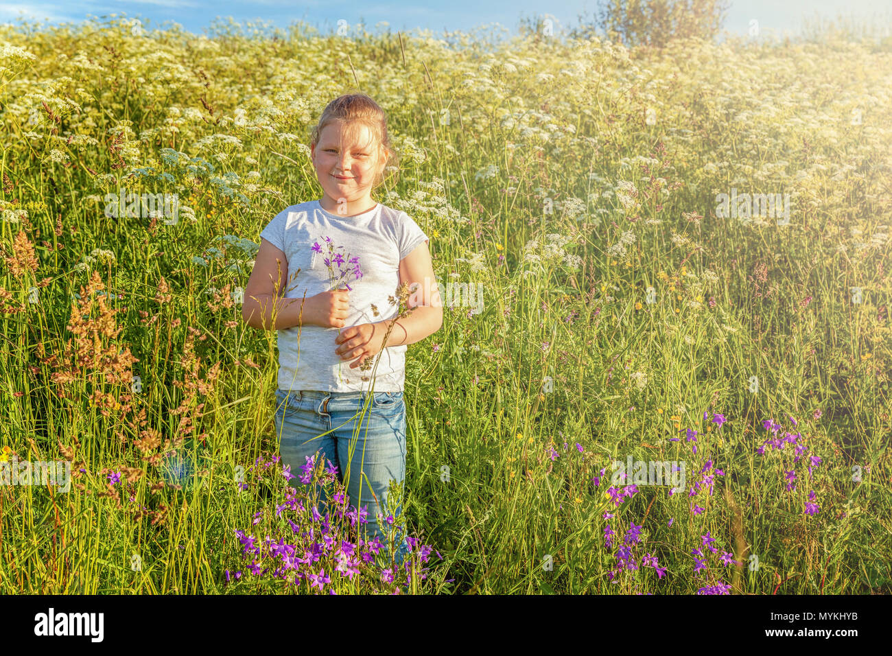Happy cute little girl stands with a bouquet of wildflowers in the park ...