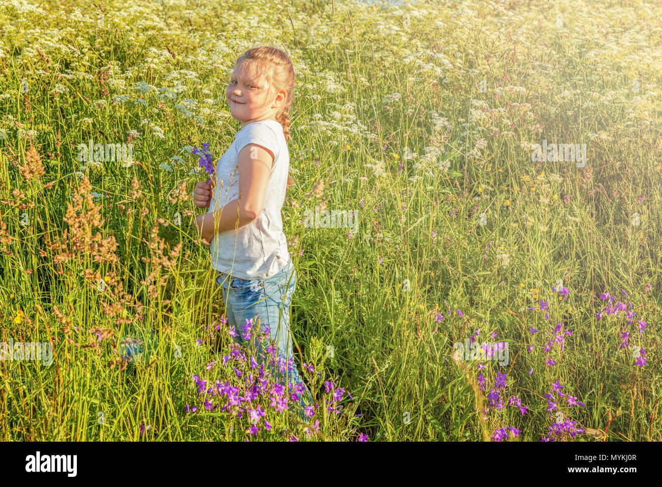 Happy cute little girl stands with a bouquet of wildflowers in the park ...