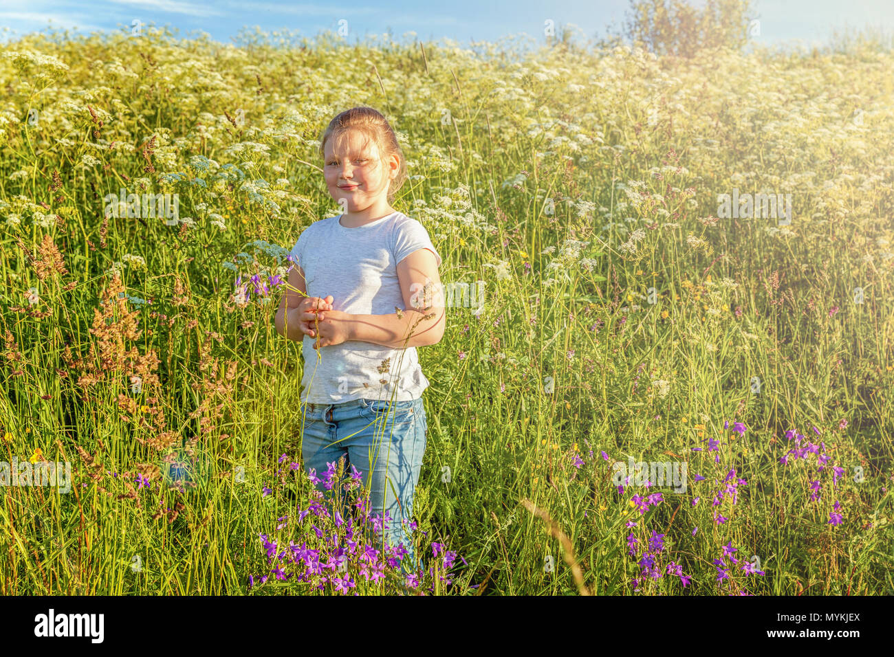 Happy cute little girl stands with a bouquet of wildflowers in the park ...