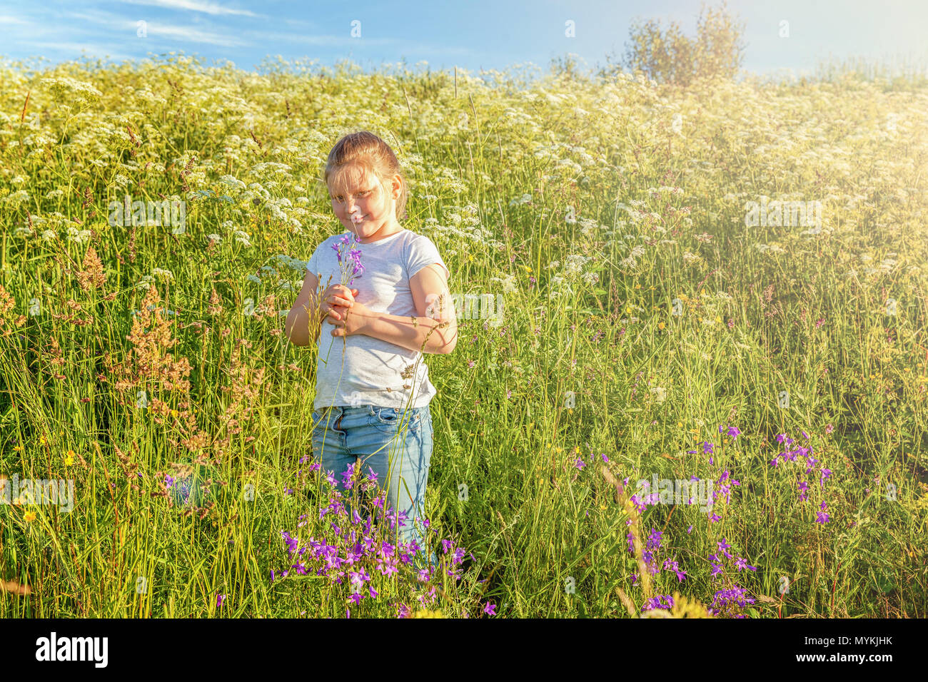 Happy cute little girl stands with a bouquet of wildflowers in the park ...