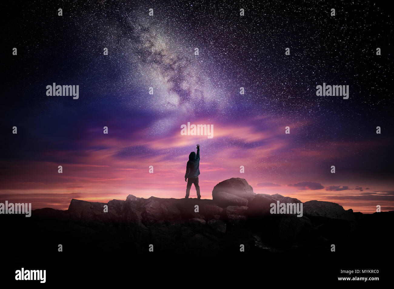 Night time long exposure landscape photography. A man standing in a high place reaching up in wonder to the Milky Way galaxy, photo composite. Stock Photo